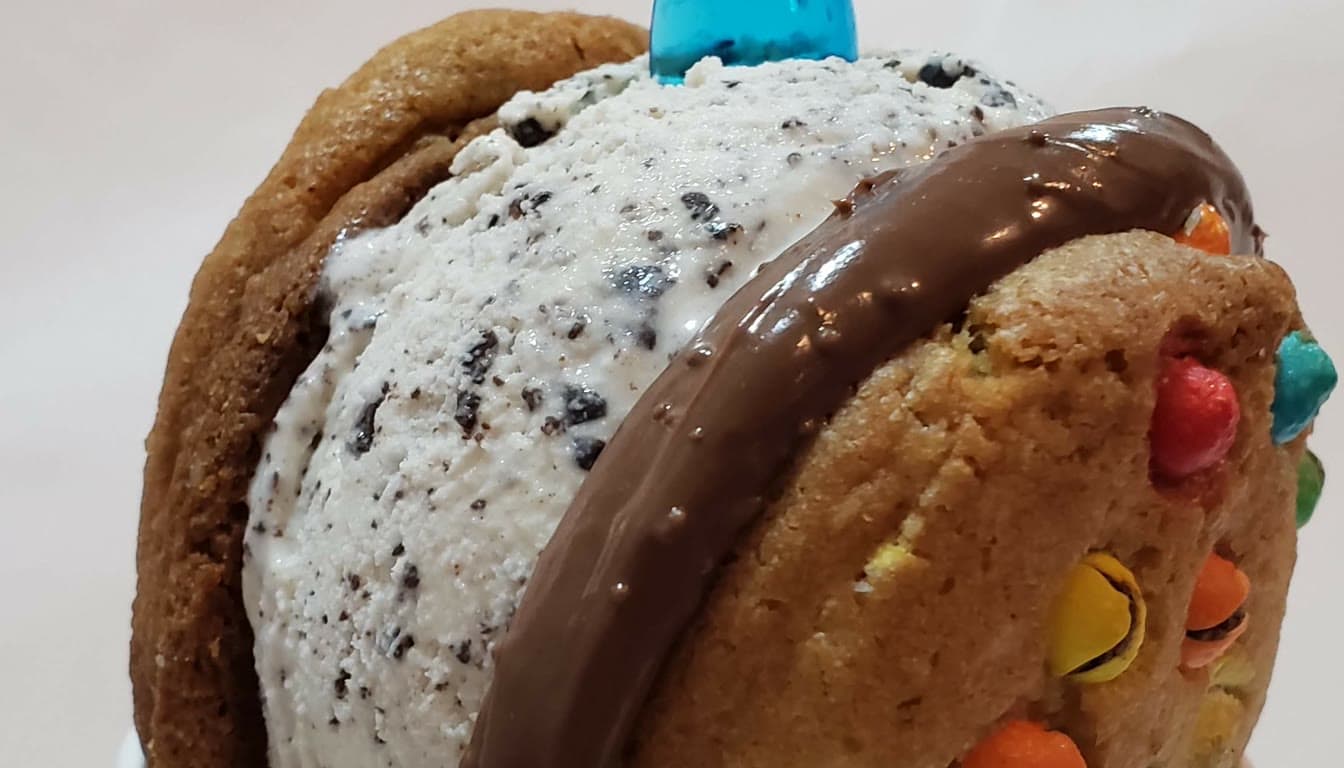 Cookeez sandwich con helado, salsa de chocolate y toppings coloridos.
